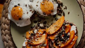 Delicious breakfast plate featuring avocado toast with fried eggs and persimmons, topped with seeds for a healthy start.