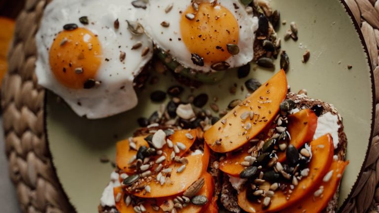 Delicious breakfast plate featuring avocado toast with fried eggs and persimmons, topped with seeds for a healthy start.